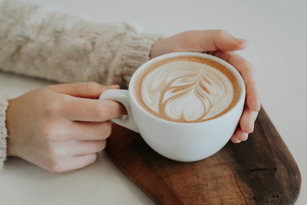 カフェラテとマグカップに添えられた女性の手