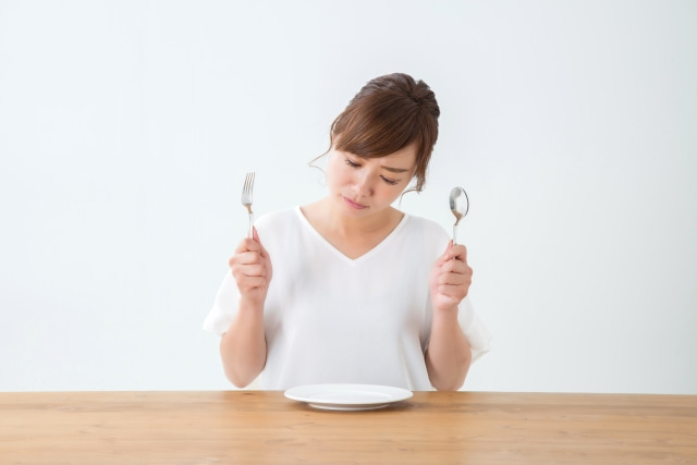 空のお皿を前にフォークとスプーンを持つ女性