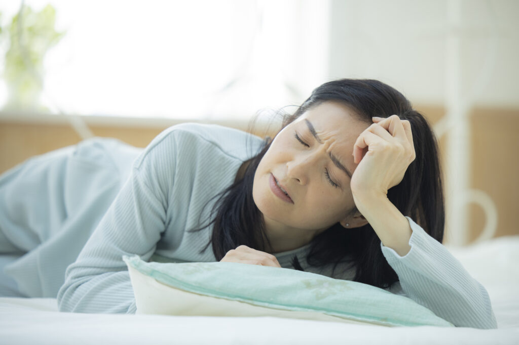 寝転びながら頭を抑える女性